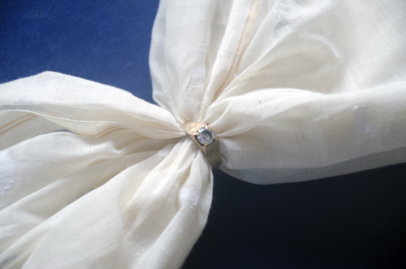 A long piece of sheer cream muslin cloth gathered through a small gold finger ring.